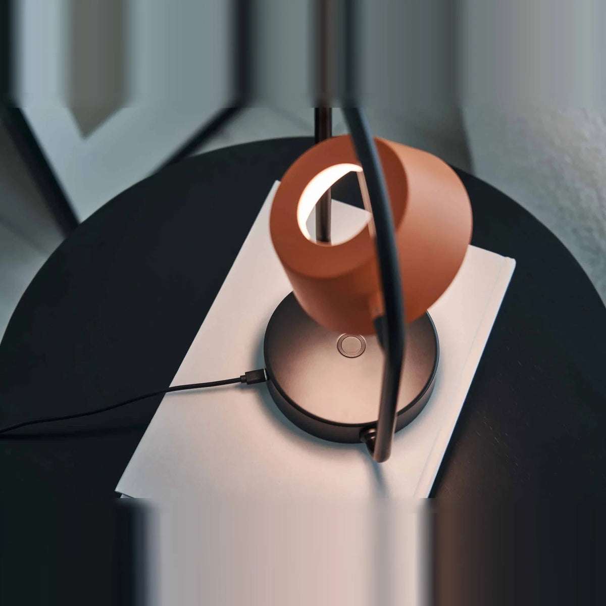 Cordless oval loop table lamp, coral orange, on a round side table