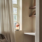 Cordless oval loop table lamp, coral orange, lit by a window