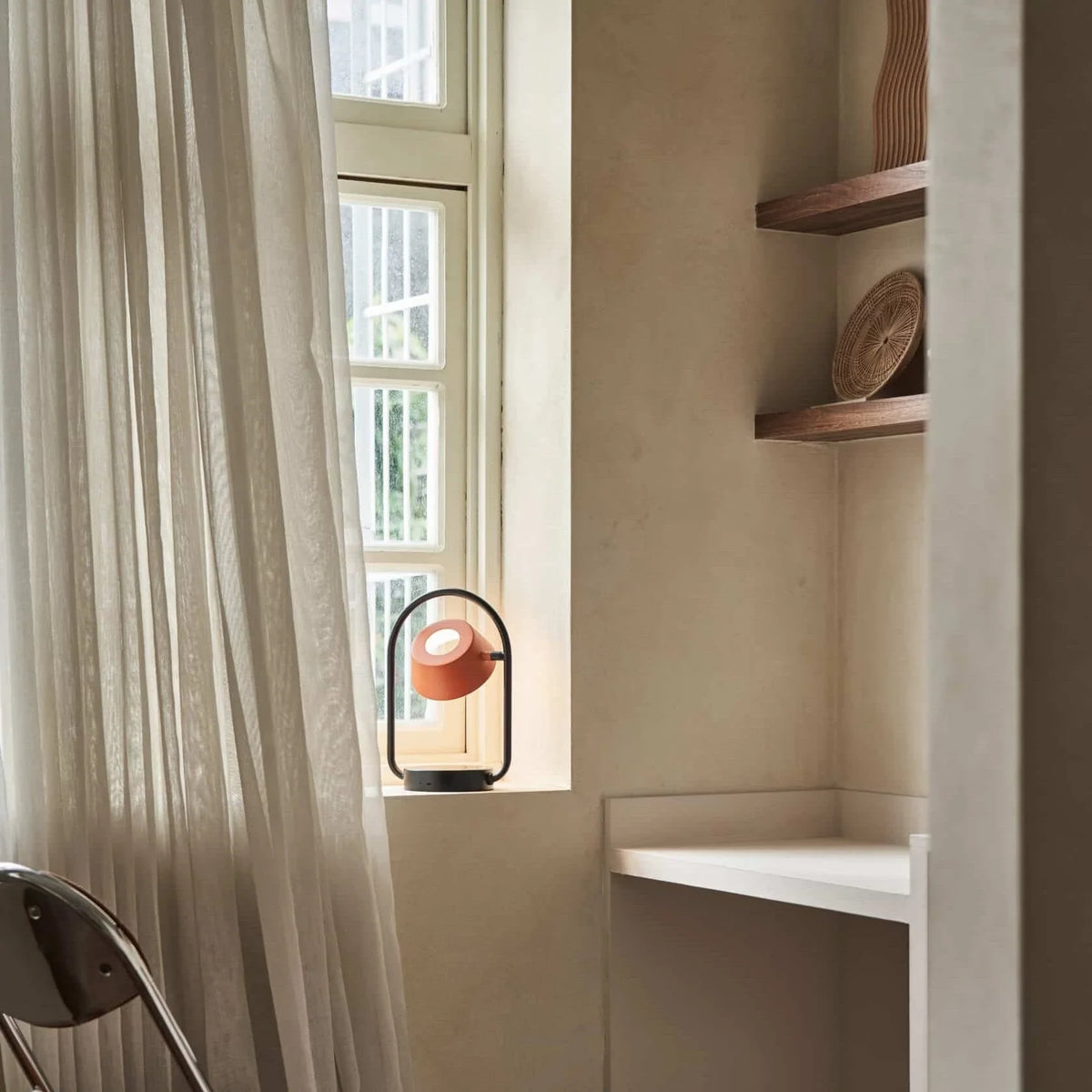 Cordless oval loop table lamp, coral orange, lit by a window