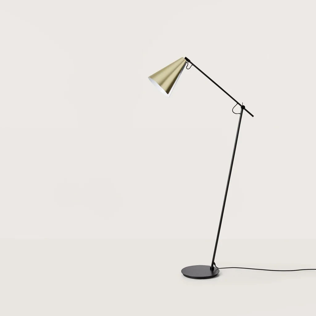 Counterbalanced arm floor lamp with conical brass shade, against a plain wall