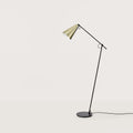 Counterbalanced arm floor lamp with conical brass shade, against a plain wall