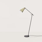 Counterbalanced arm floor lamp with conical brass shade, against a plain wall