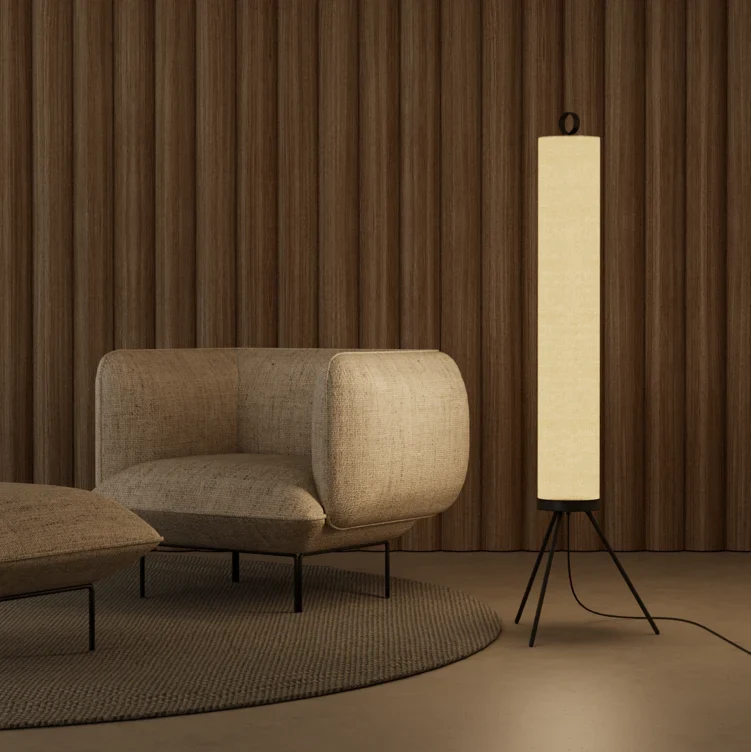 Cream linen tube floor lamp with black tripod base, beside an armchair
