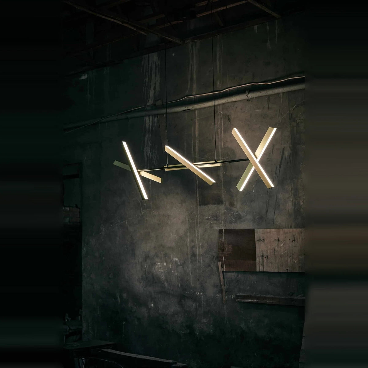 Crossed bar linear LED pendant, lit against a dark wall