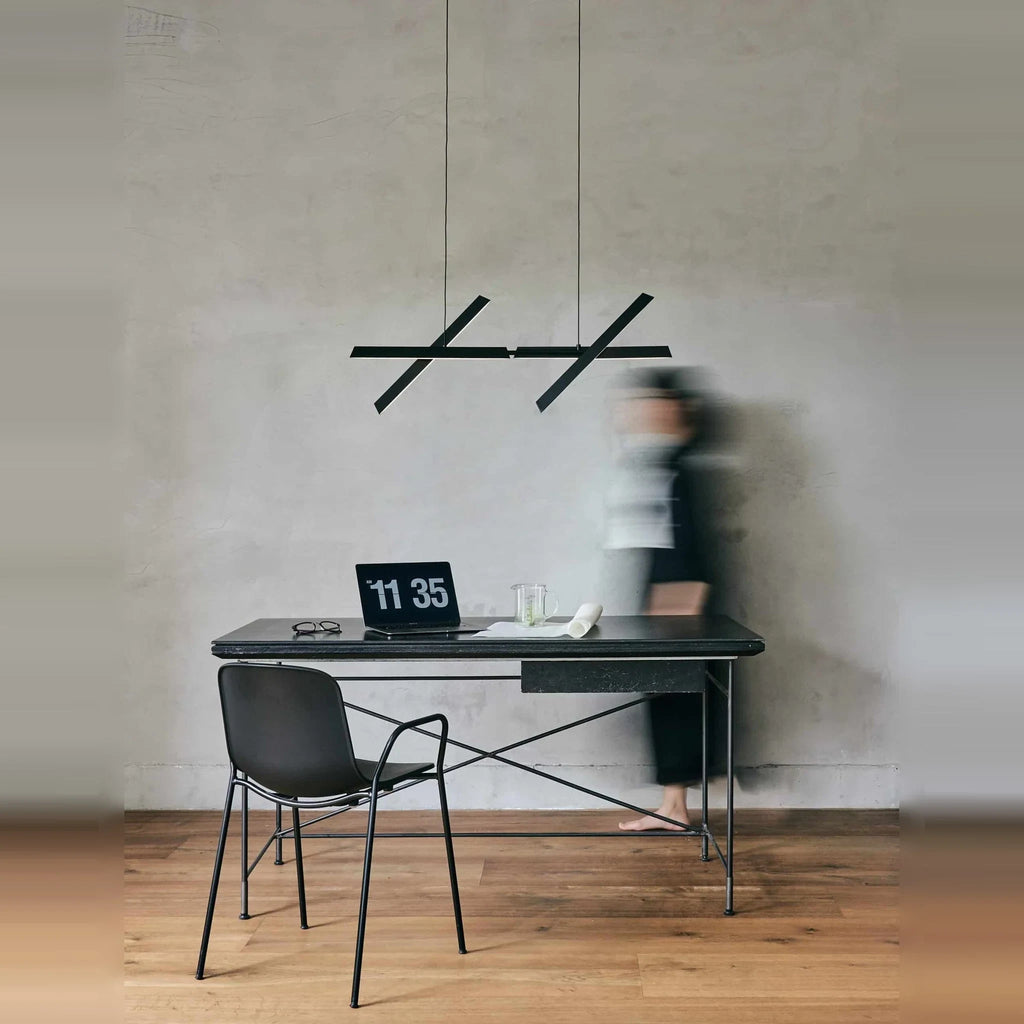 Crossed bar linear LED pendant, above a desk with a person passing