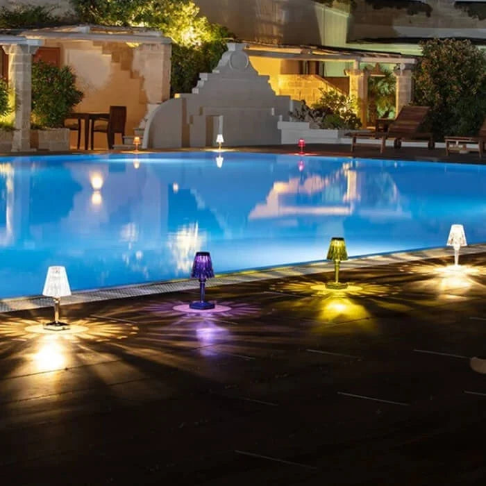 Crystal-effect rechargeable table lamp, several colours lit beside a pool at night