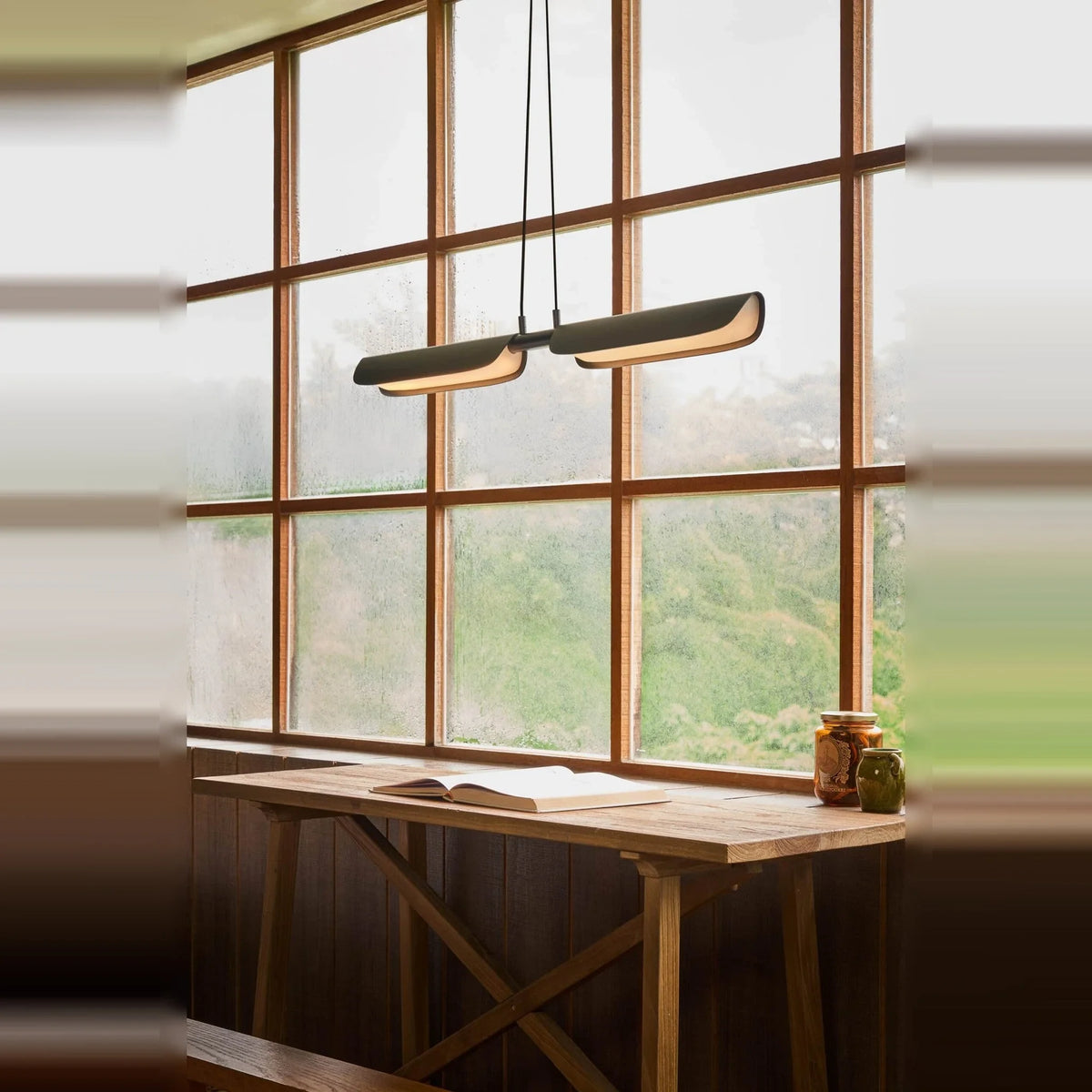 Curved shade linear LED pendant, lit above a desk by a window