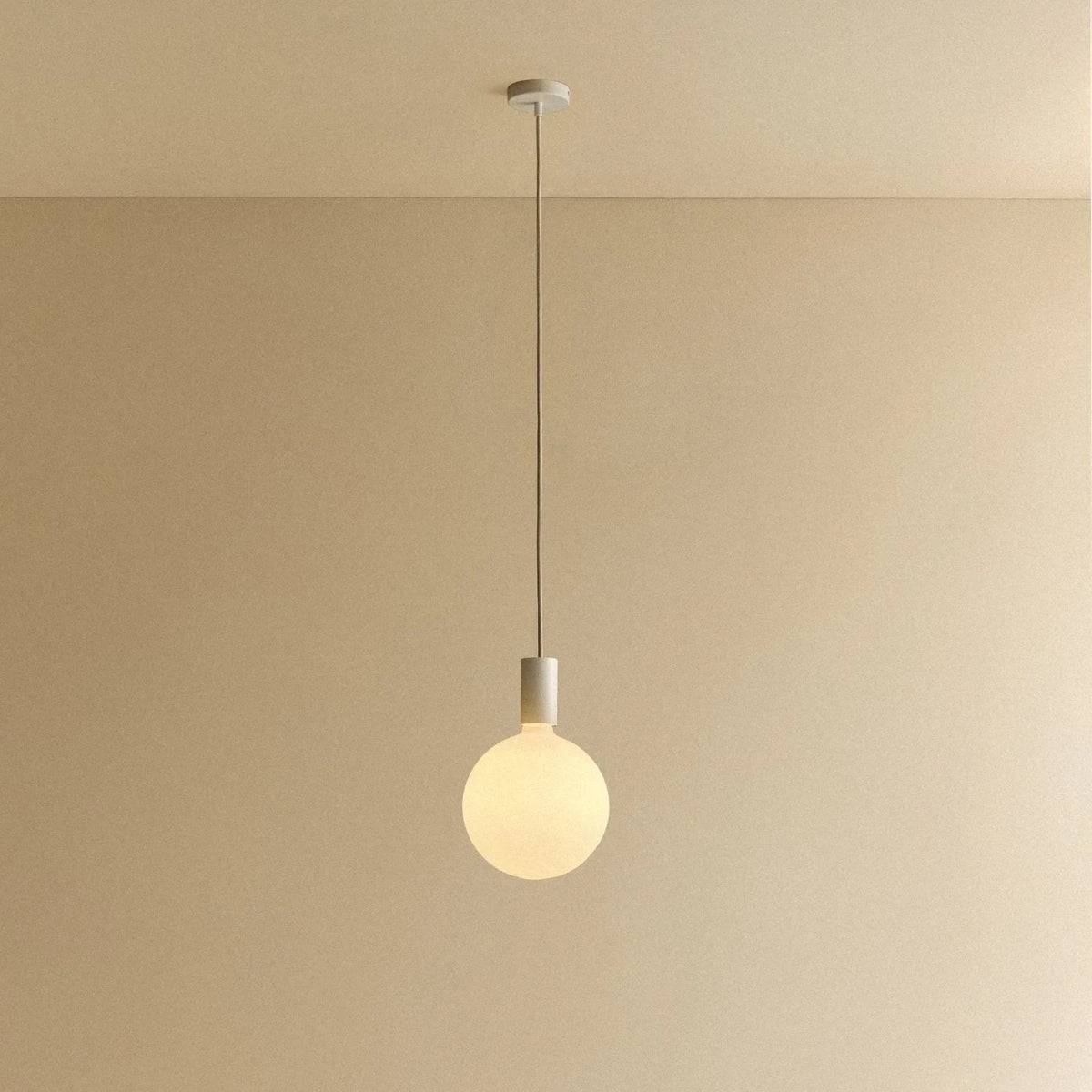 Cylinder pendant with matt white globe bulb, chalk, lit, against a plain wall