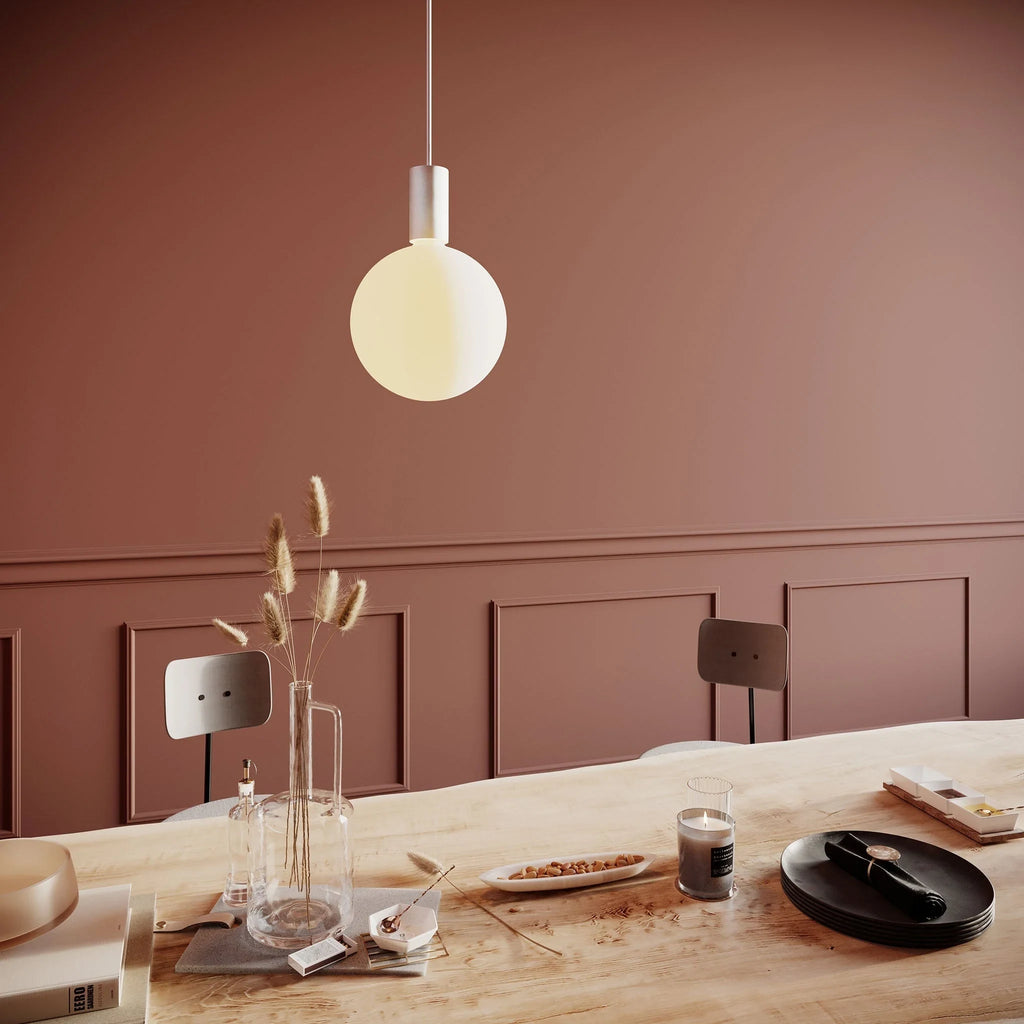 Cylinder pendant with matt white globe bulb, chalk, above a dining table against a terracotta wall