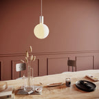 Cylinder pendant with matt white globe bulb, chalk, above a dining table against a terracotta wall