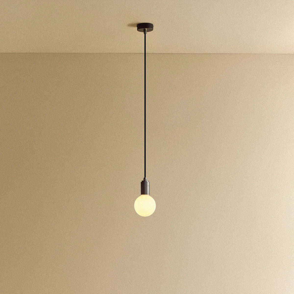 Dim-to-warm globe pendant, graphite, lit, against a plain wall