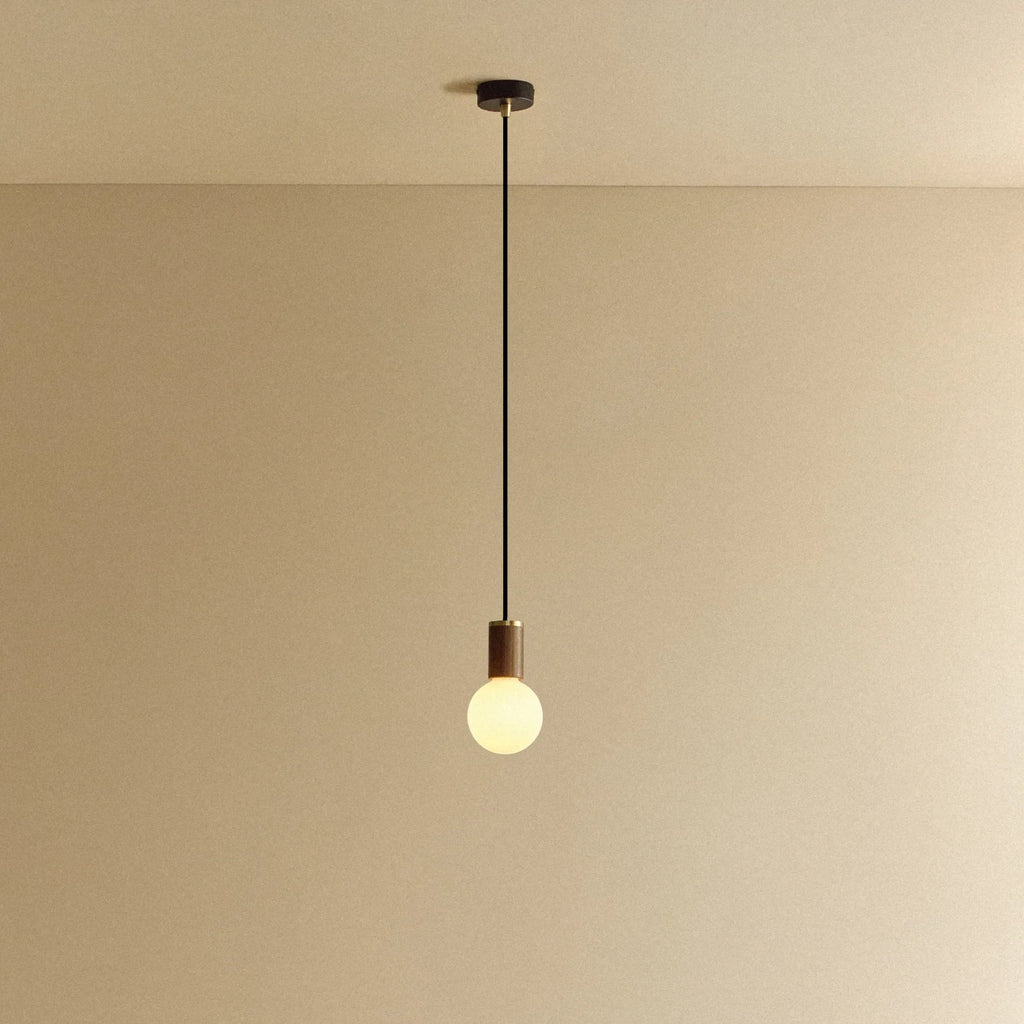 Dim-to-warm globe pendant, walnut, lit, against a plain wall