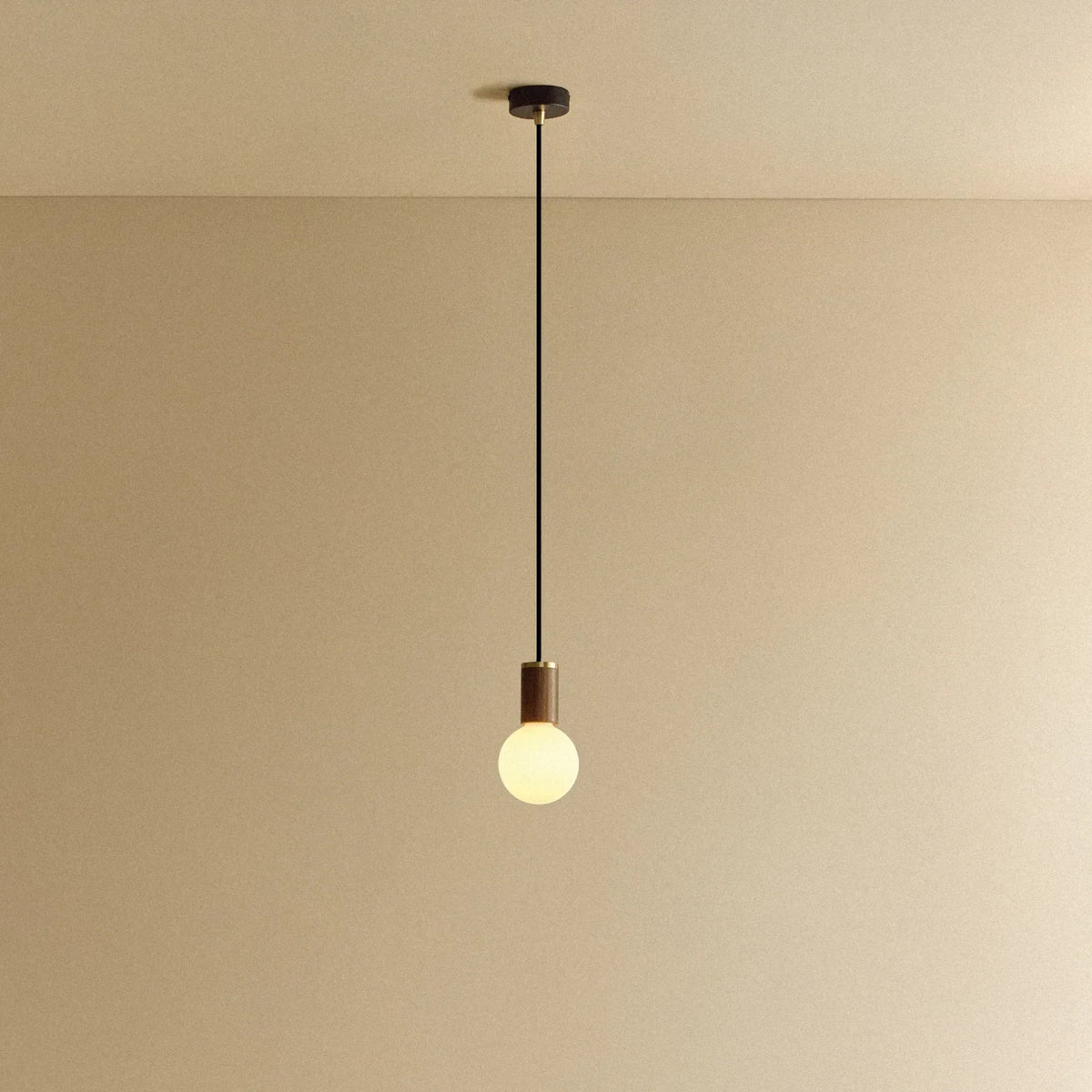 Dim-to-warm globe pendant, walnut, lit, against a plain wall