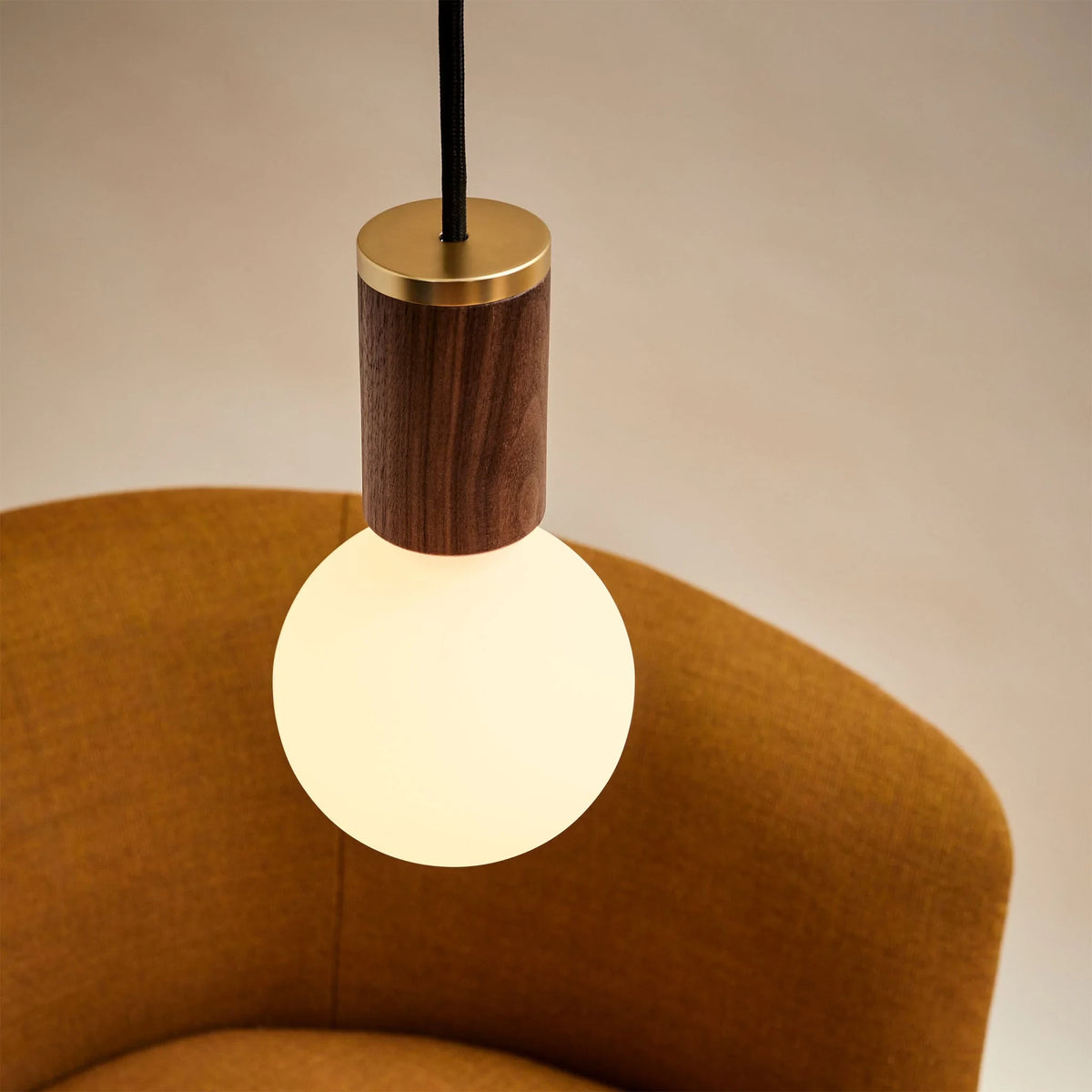 Dim-to-warm globe pendant, walnut, close-up of the lit globe above an armchair