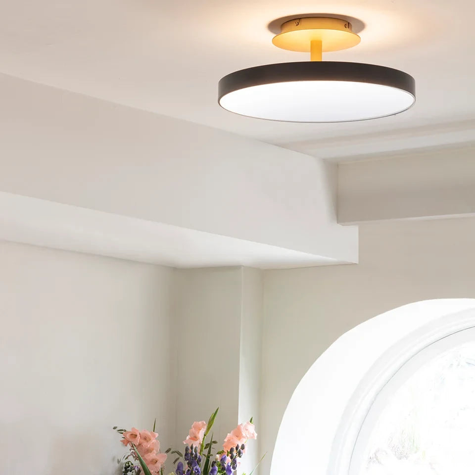 Disc LED ceiling light with brass stem, in pearl white, in a bright room