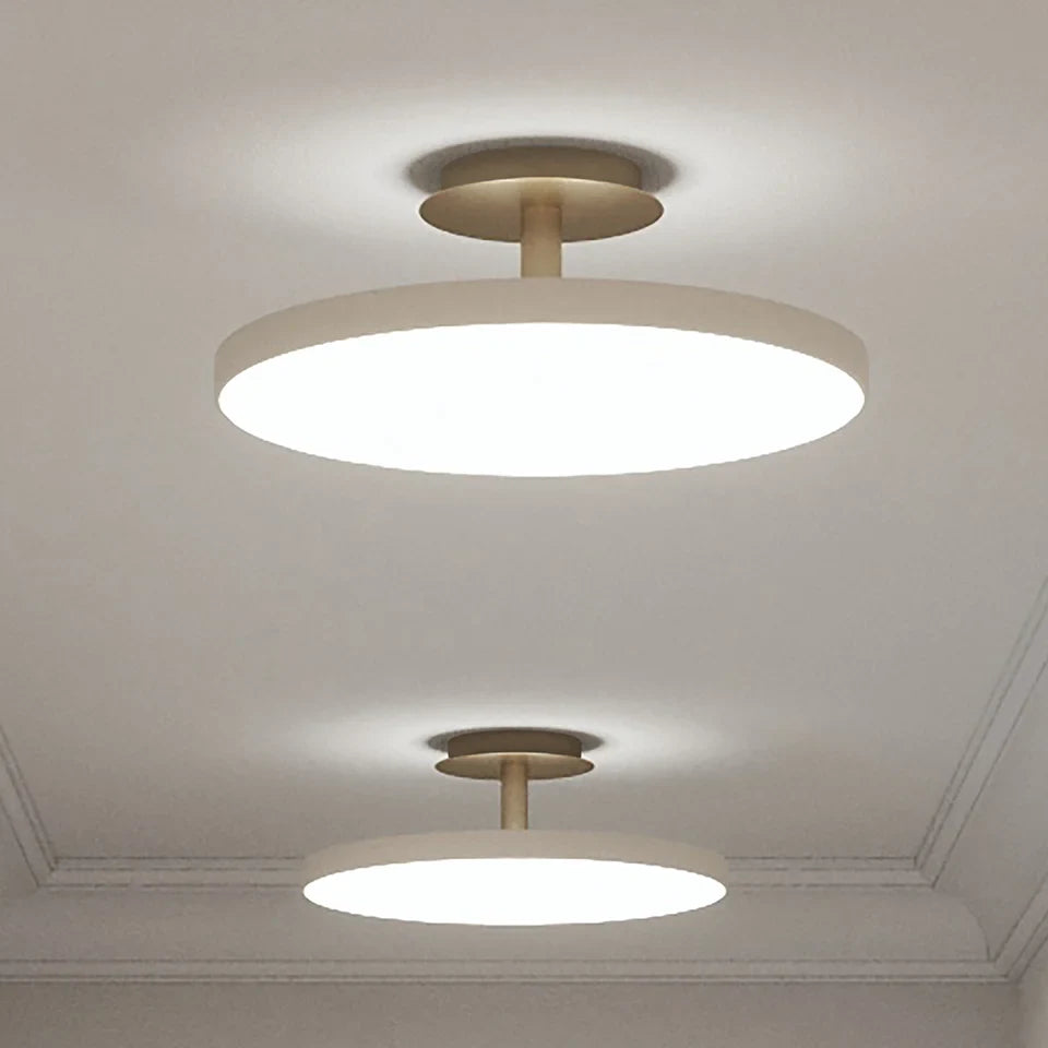 Disc LED ceiling light with brass stem, two sizes in a pale room