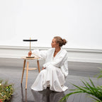 Disc-top LED table lamp with brass stem, in black, on a stool beside a seated person