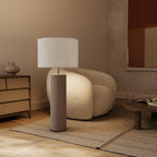 Extra-tall hand-painted ceramic cylinder table lamp, in grey, beside a lounge chair, with a shade (sold separately)