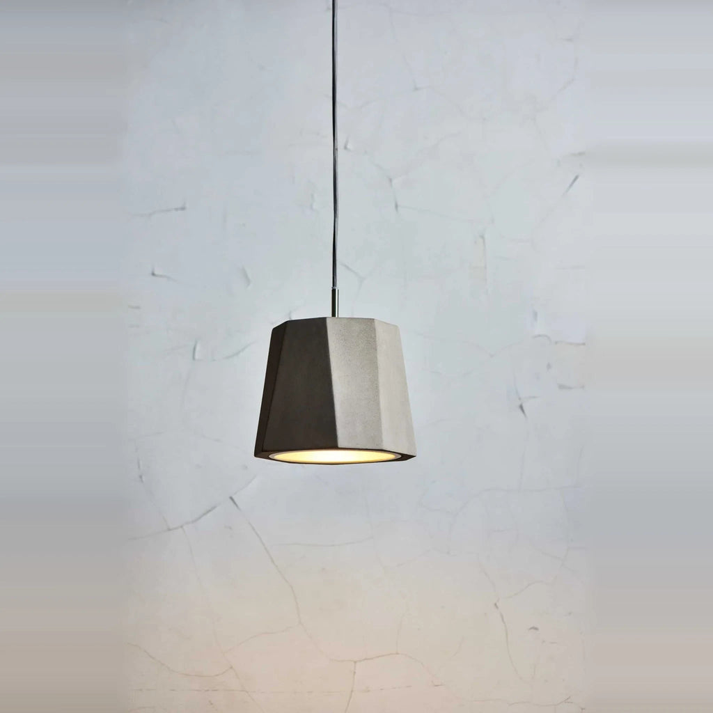Faceted concrete pendant, single shade lit against a pale wall
