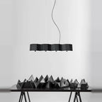 Faceted metal linear pendant, in black above a sculptural table display