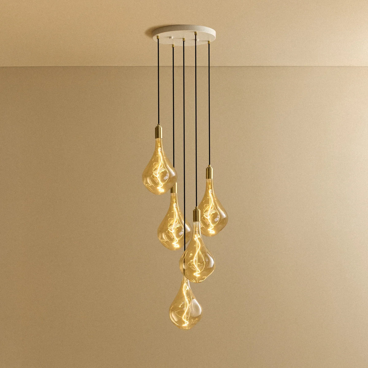 Five-drop cluster pendant with large tinted sculptural bulbs, brass, lit, on a white canopy