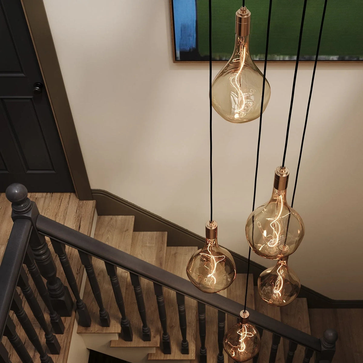 Five-drop cluster pendant with large tinted sculptural bulbs, brass, above a staircase