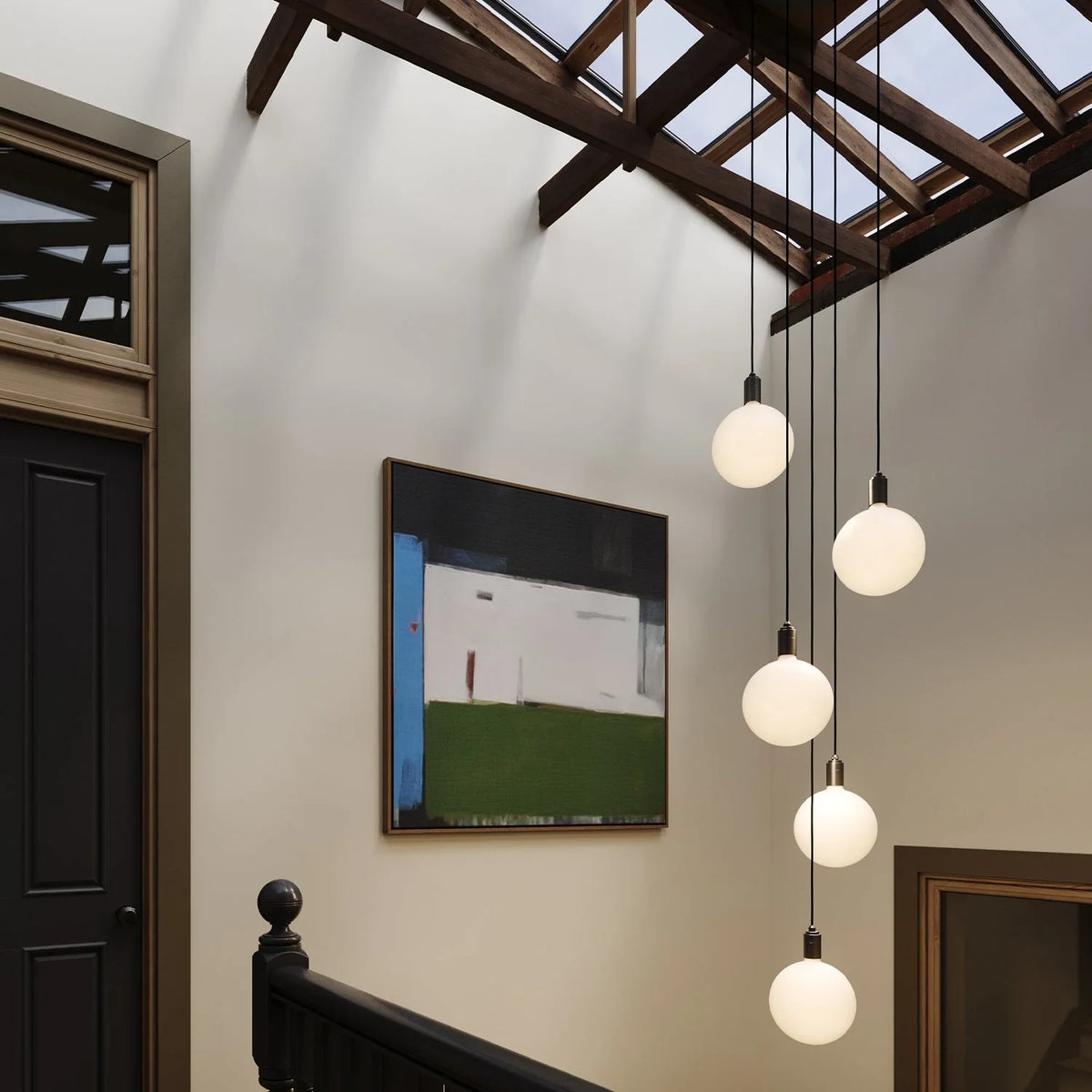 Five-drop cluster pendant with opal globe bulbs, brass, in a stairwell under a skylight