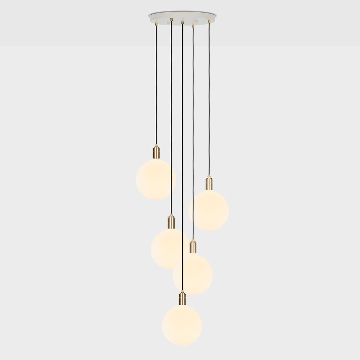 Five-drop cluster pendant with opal globe bulbs, brass, lit, on a pale background