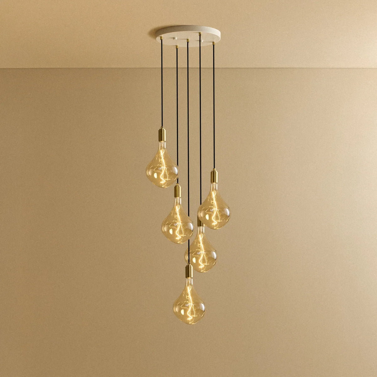 Five-drop cluster pendant with tinted sculptural bulbs, brass, lit, on a white canopy