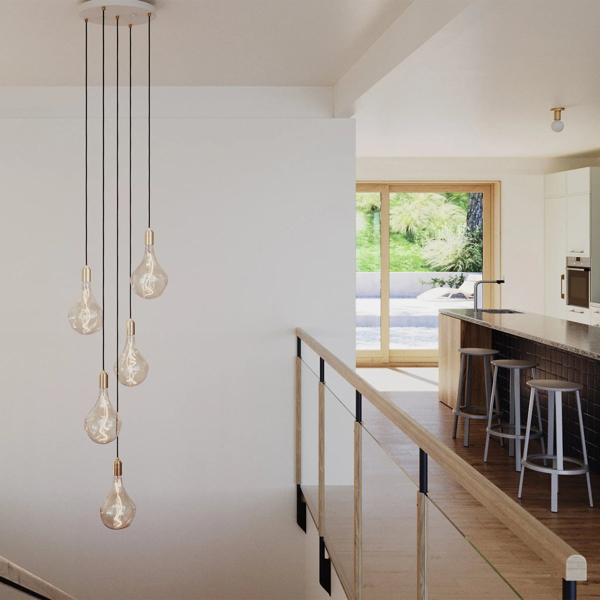 Five-drop cluster pendant with tinted sculptural bulbs, brass, in a double-height kitchen