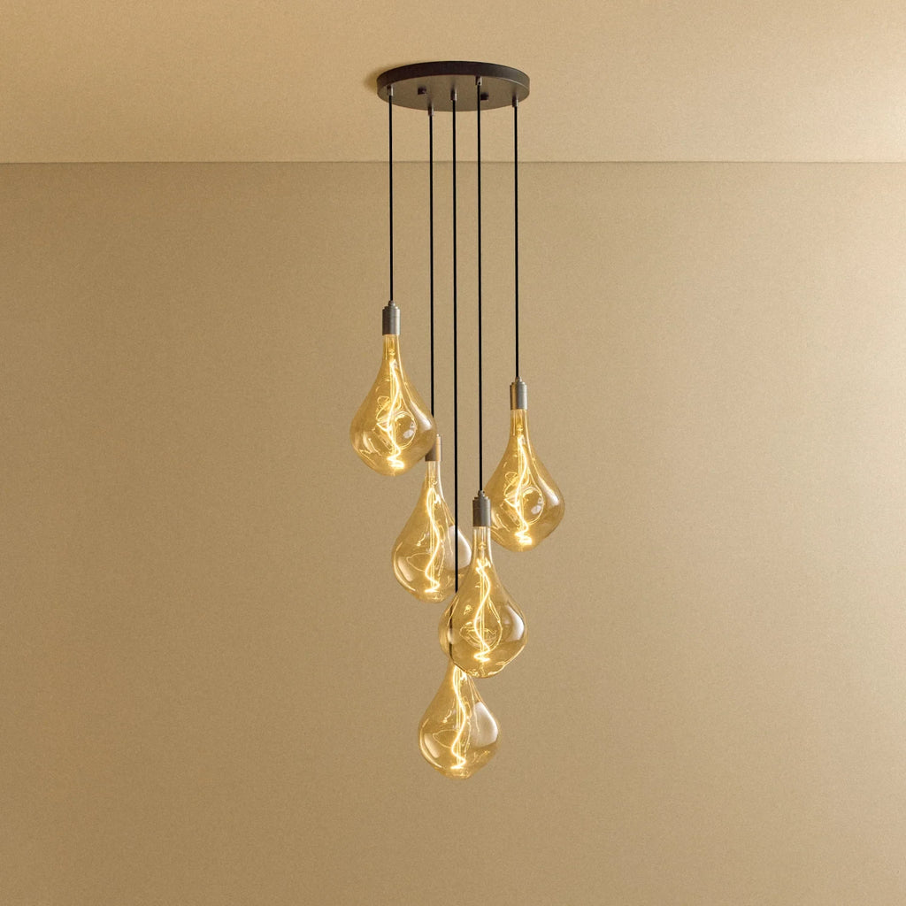 Five-drop cluster pendant with tinted sculptural bulbs, graphite, lit, against a plain wall