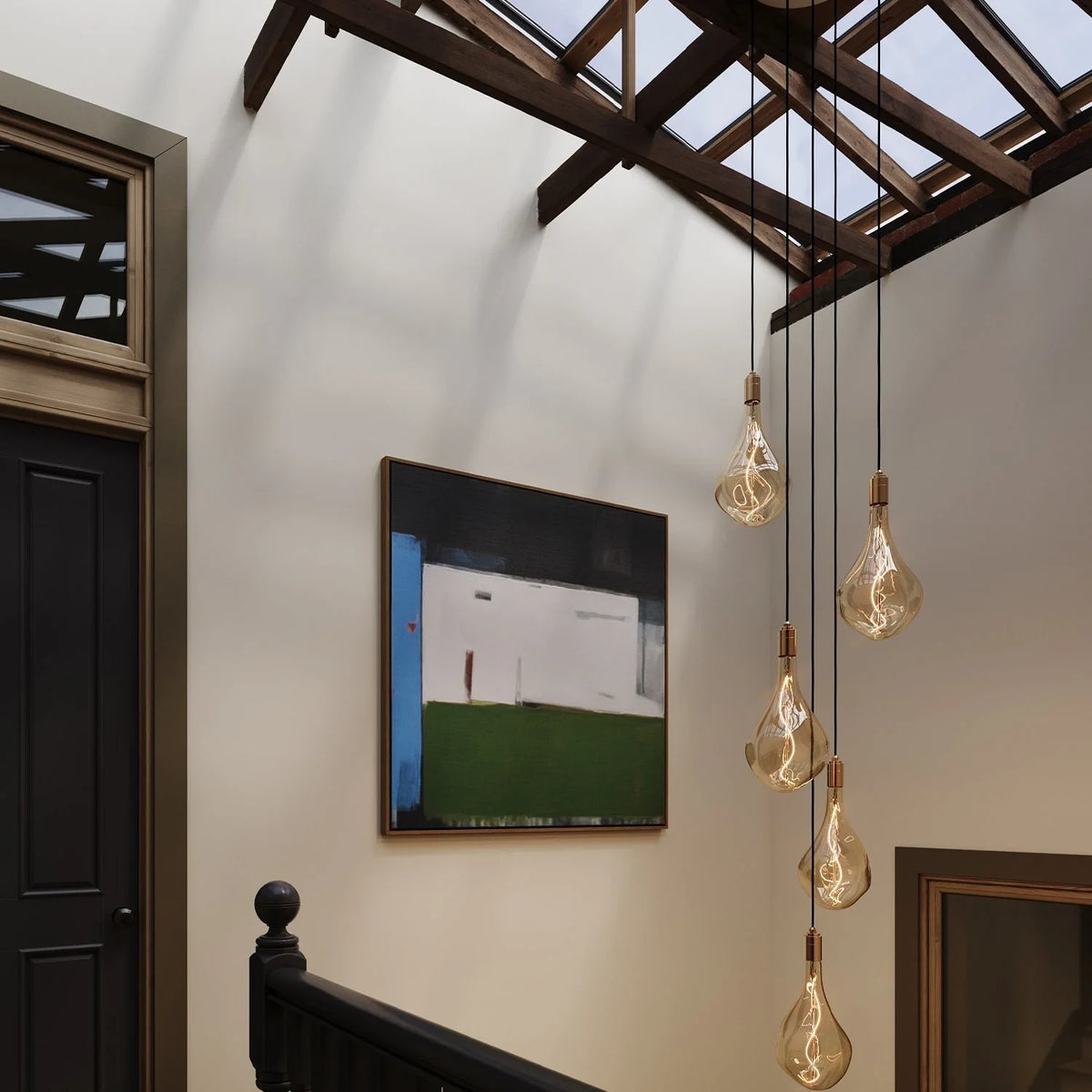 Five-drop cluster pendant with tinted sculptural bulbs, graphite, in a stairwell under a skylight