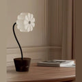 Flower glass shade lamp with curved stem and marble pot, on a wooden table by a window