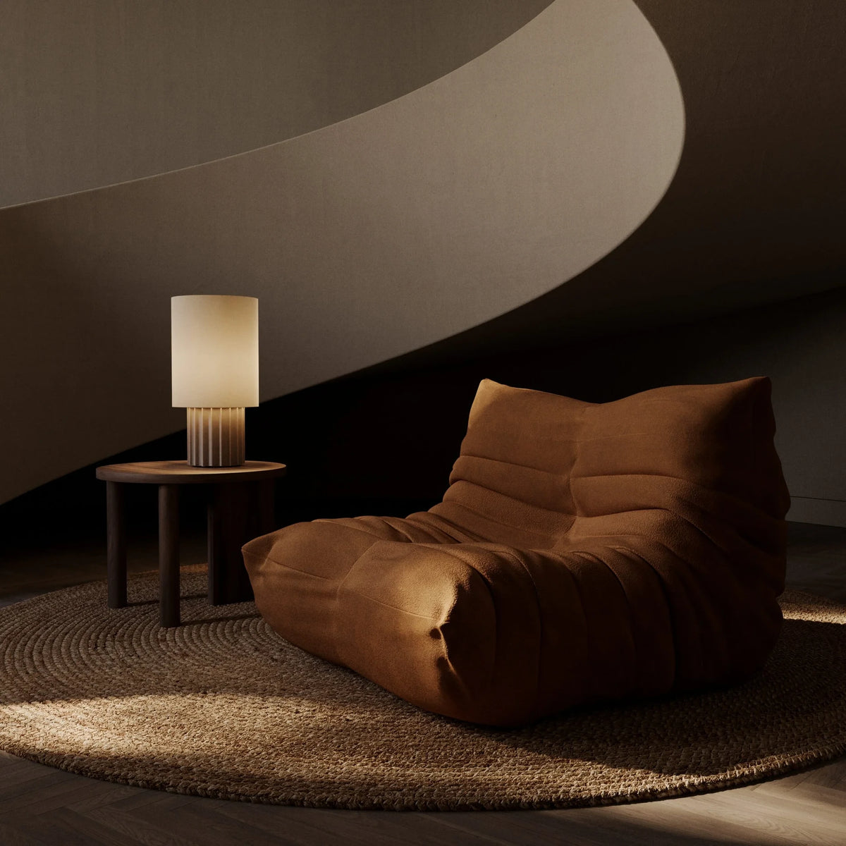 Fluted ceramic drum table lamp base, lit beside a lounge chair, with a shade (sold separately)