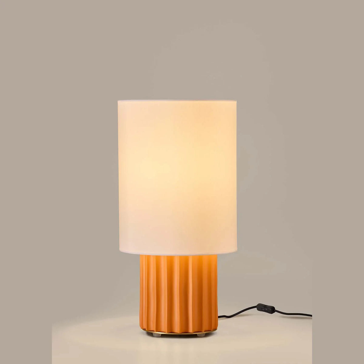 Fluted ceramic drum table lamp base, in orange, lit, with a shade (sold separately)