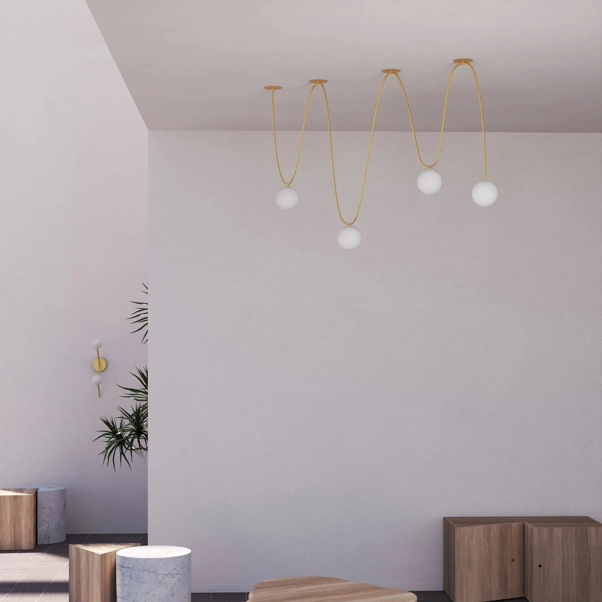 Free-form looping cable pendant with five white globes, brushed brass, in a bright room with a plant and wooden stools