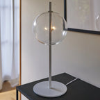 Mouth-blown glass globe table lamp on a slim steel stem, with clear glass, on a side table