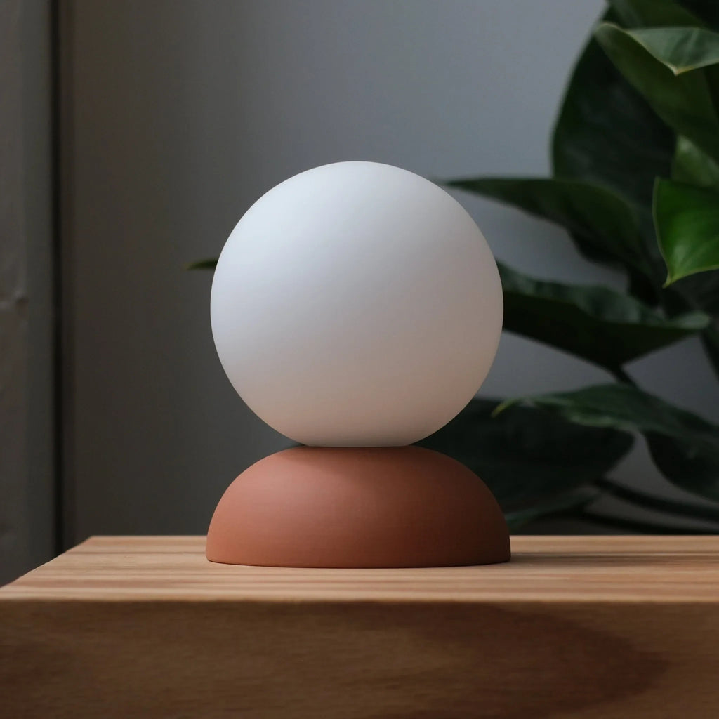 Glazed stoneware globe table lamp, in terracotta on a wooden shelf