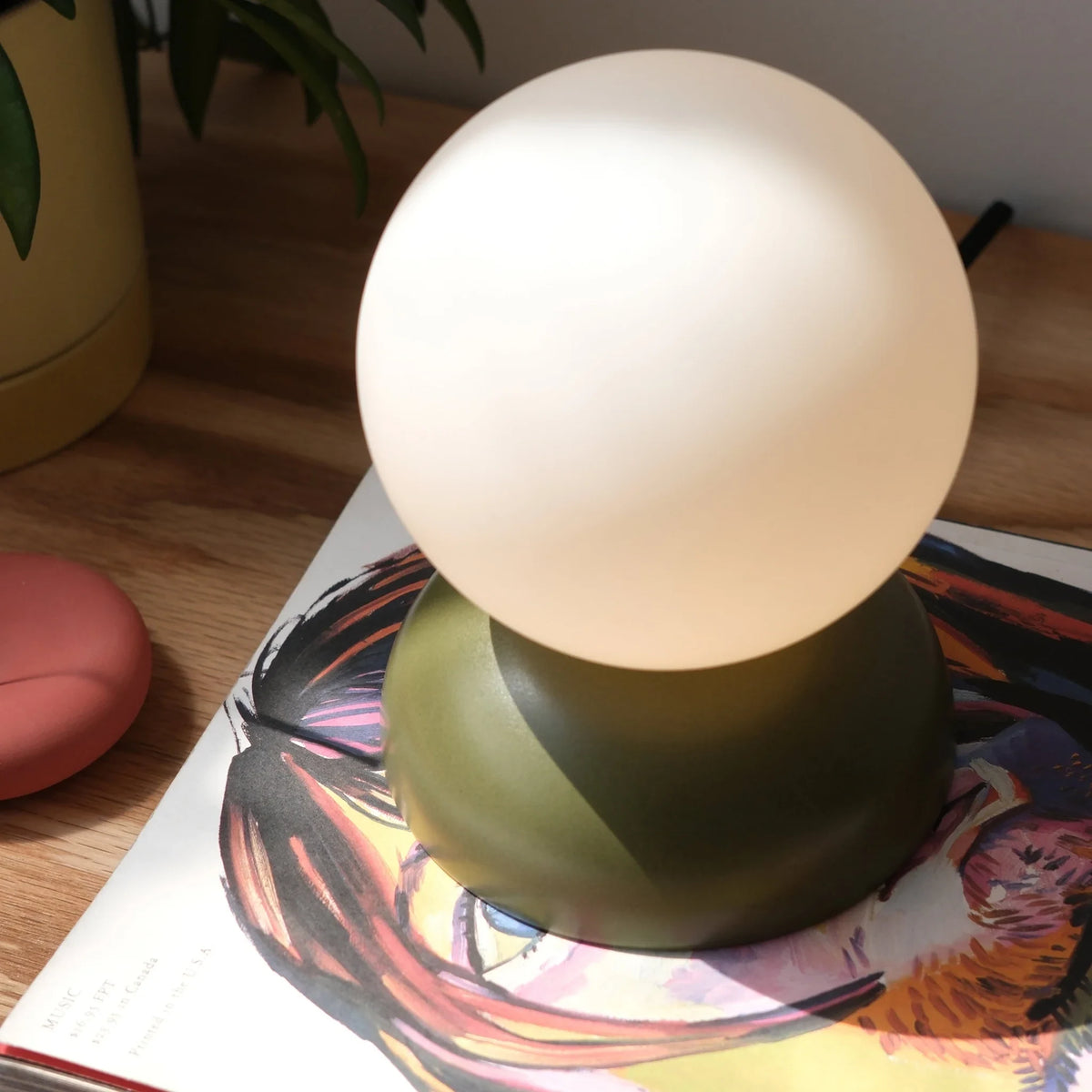 Glazed stoneware globe table lamp, in moss green on a table