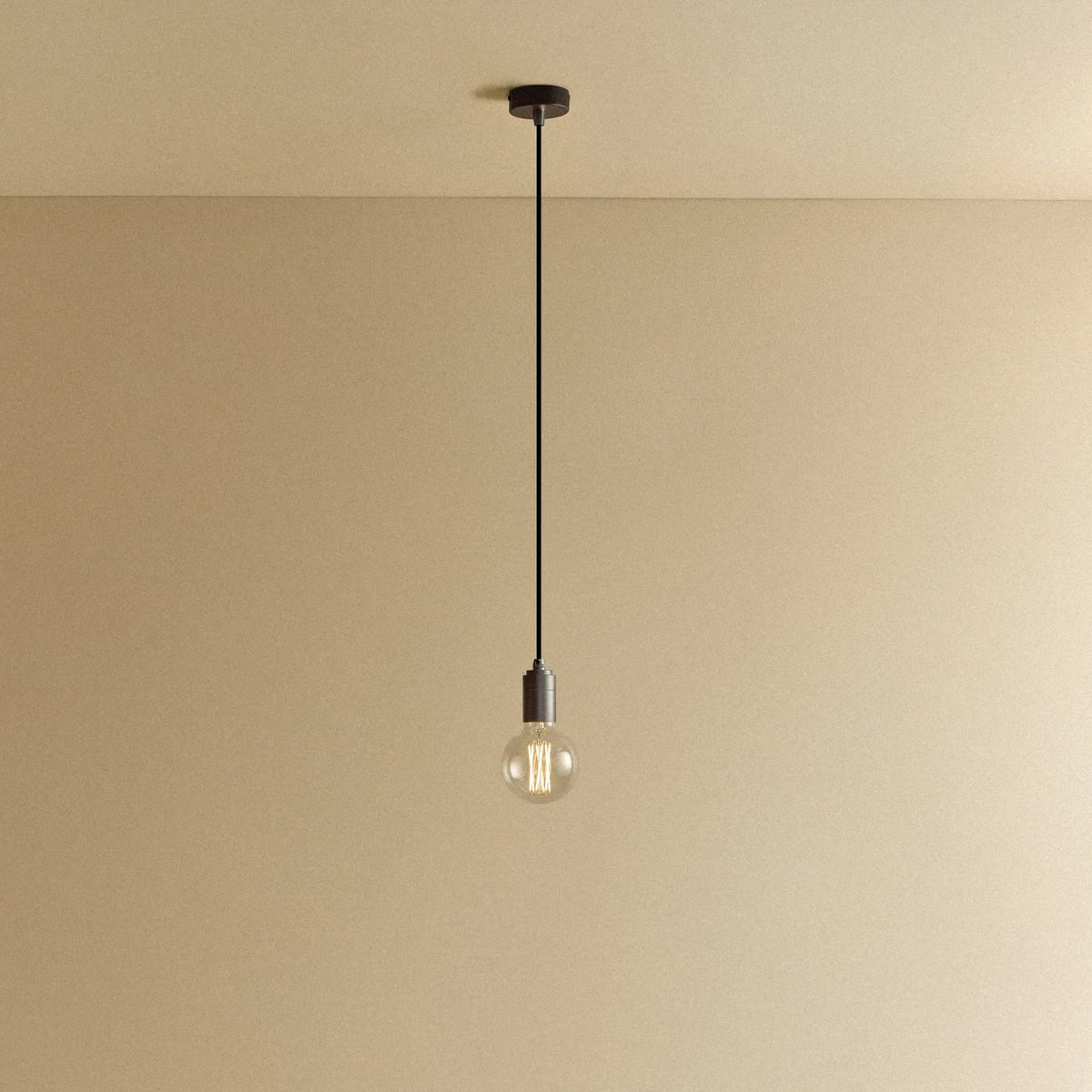 Graphite pendant with non-tinted glass filament bulb, lit, against a plain wall