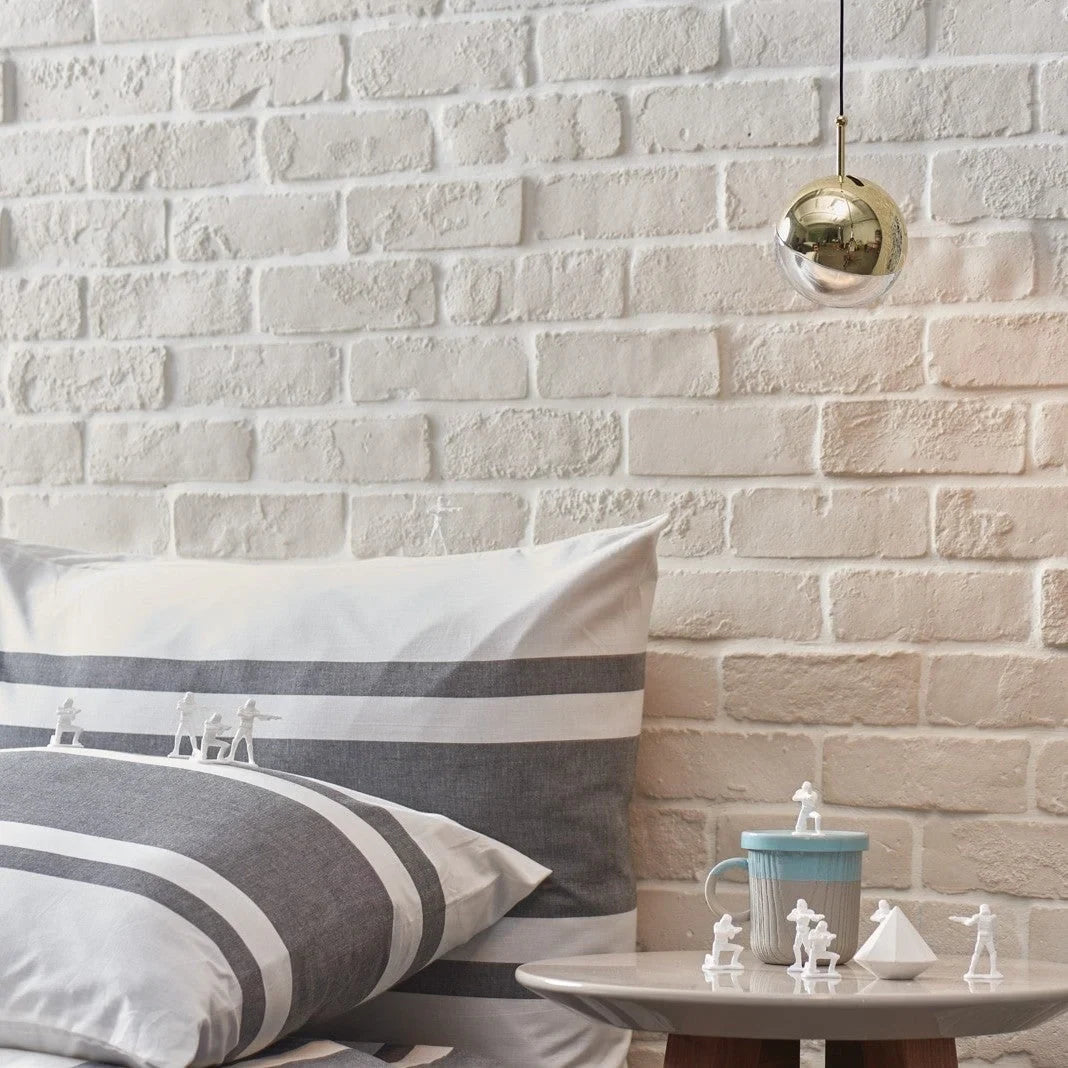 Half-capped glass globe LED pendant, in brass beside a brick wall