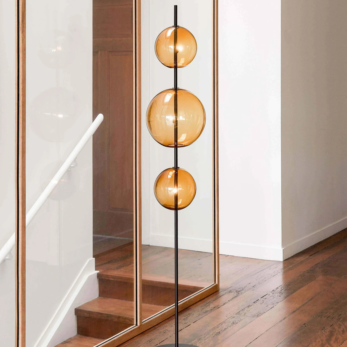 Modular hand-blown glass globe floor lamp, in amber glass beside a staircase