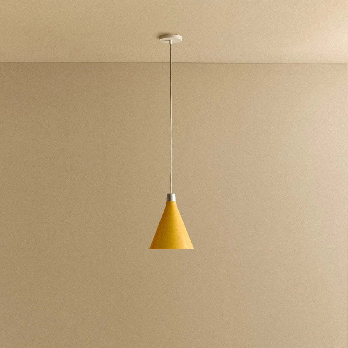 Small yellow hand-spun steel cone pendant, against a plain wall