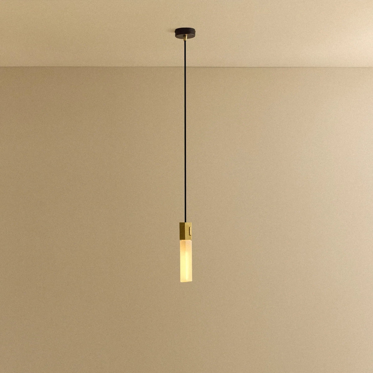 Hexagonal cast brass pendant with glass bulb, lit, against a plain wall