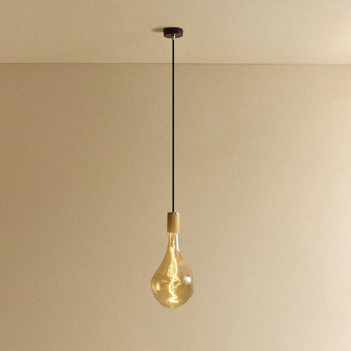 Large teardrop tinted glass pendant, oak, lit, against a plain wall