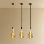 Set of three large teardrop tinted glass pendants, graphite, set of three lit, against a plain wall