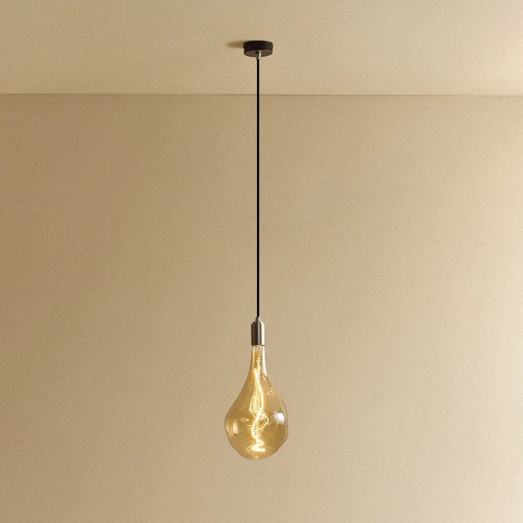 Large tinted sculptural bulb pendant, stainless steel, lit, against a plain wall