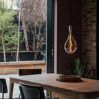 Large tinted sculptural bulb pendant, stainless steel, above a wooden dining table