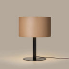 Leather drum shade table lamp, matte black base, lit, with a light brown leather shade
