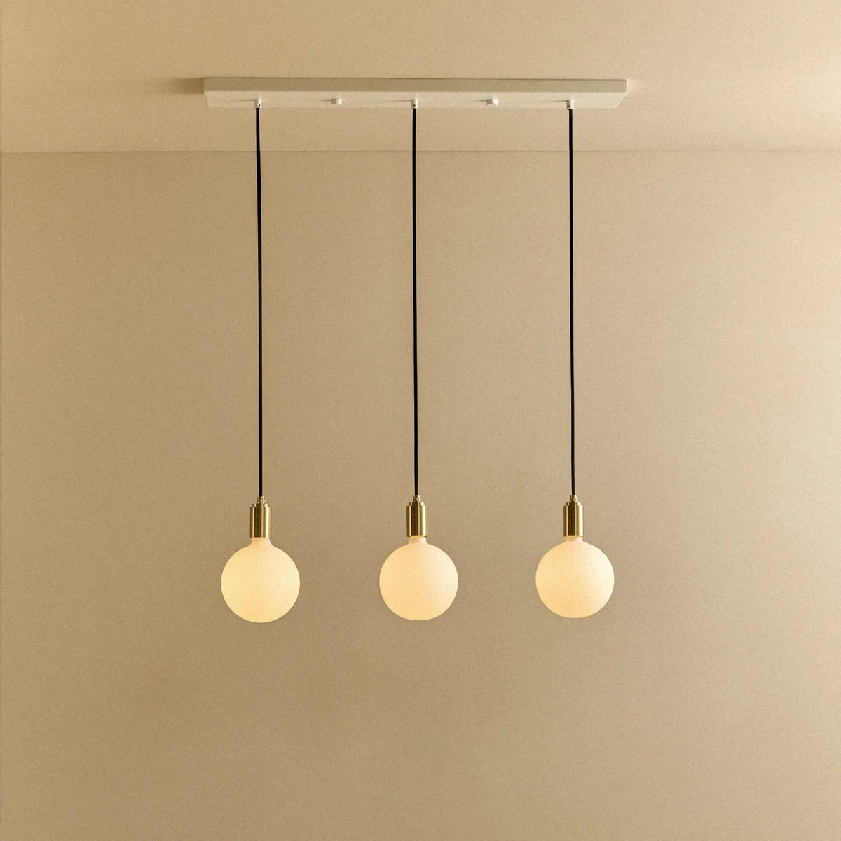Linear triple opal globe pendant, with white canopy against a plain wall